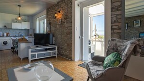 A modern living room with a stone wall, a television, a sofa, and a view of the outdoors. - Stunning private villa for 4 people with WIFI, TV and pets allowed (Le Vourch)