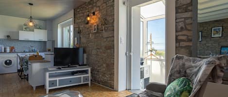 Ein modernes Wohnzimmer mit Steinwand, Fernseher, Sofa und Blick ins Freie.