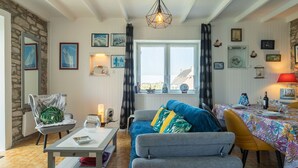 A cozy living room with a sofa, armchairs, a coffee table, and a dining area with a table set for two. There are framed pictures on the walls, a window with curtains, and a hanging light fixture. - Stunning private villa for 4 people with WIFI, TV and pets allowed (Le Vourch)