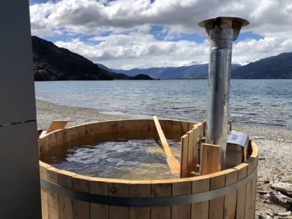 Un bain à remous en bois, doté d’une structure métallique, installé sur une plage au bord d’un lac.