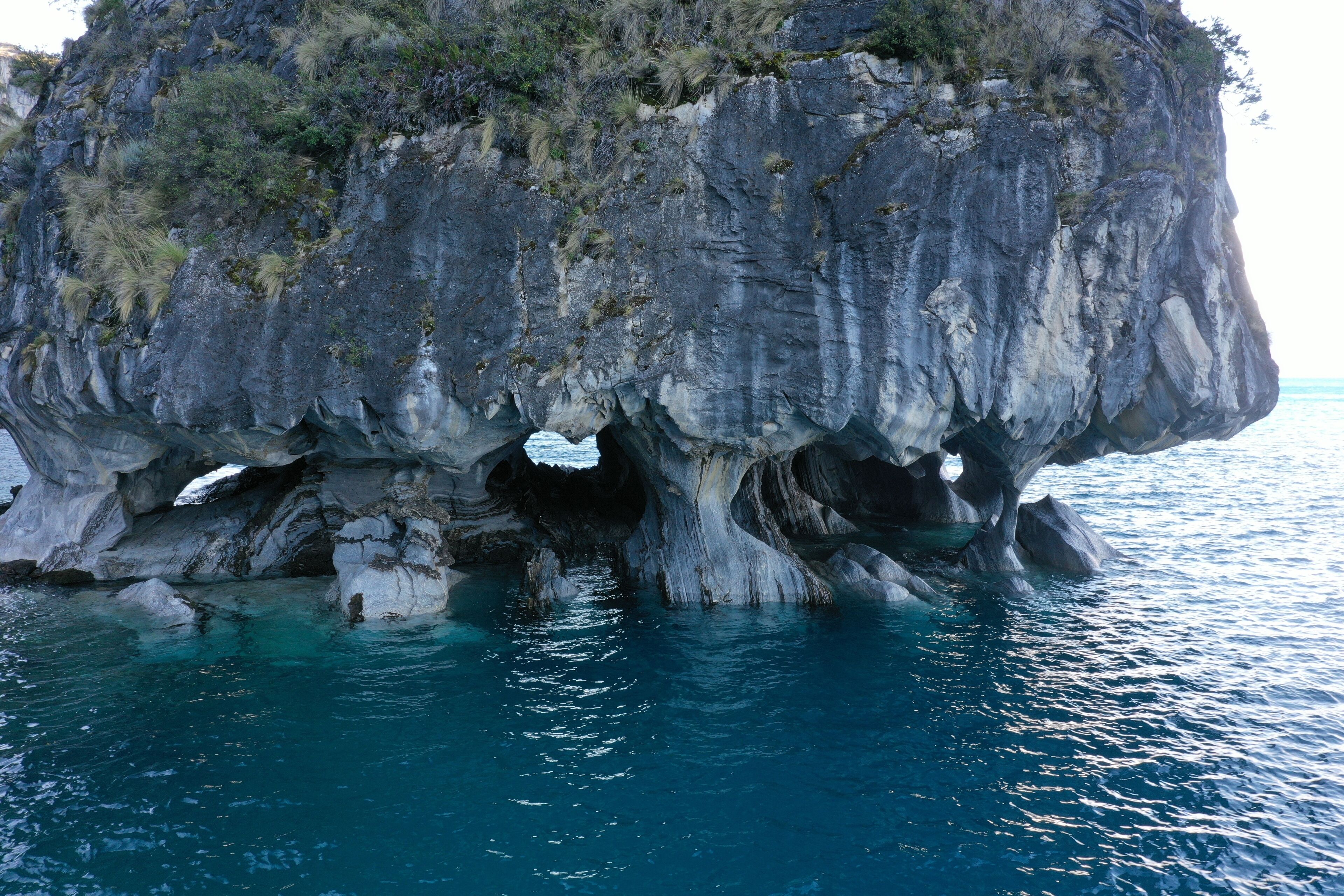 Una gran formación rocosa con una abertura similar a una cueva, rodeada de agua cristalina azul.