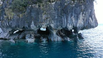Una gran formación rocosa con una abertura similar a una cueva, rodeada de agua cristalina azul.