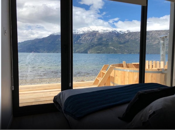 A bedroom with a large window overlooking a lake and mountains.