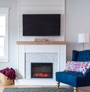 Una sala de estar moderna con chimenea, televisor montado y un sofá azul.