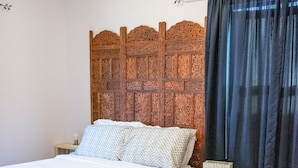 A bedroom with a wooden headboard, a bed with white bedding, a nightstand with a lamp, and a chair. - Blue Cottage in the heart of Tulsa (Tulsa)