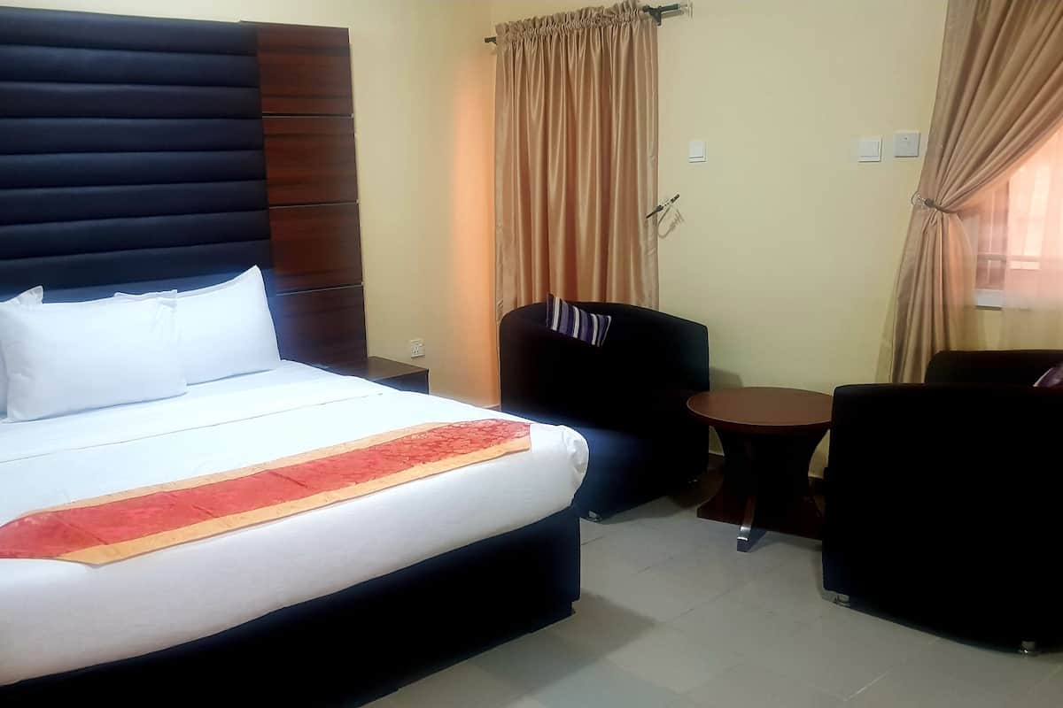A hotel room with a large bed, a small round table, a chair, and a sofa.