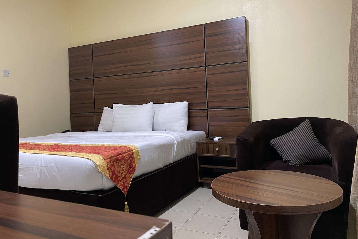A hotel room with a large bed, a wooden headboard, a small table, a chair, and a nightstand.