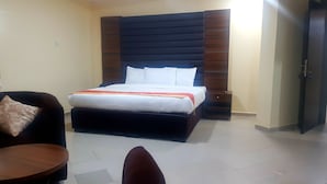 A hotel room with a bed, a chair, a small table, and a wardrobe. - Blue Springs Hotel (Abuja)