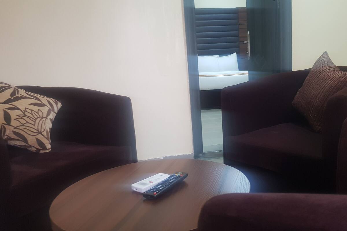 A room with two dark-colored sofas, one with a floral-patterned pillow, and a small wooden table with a remote control on it.