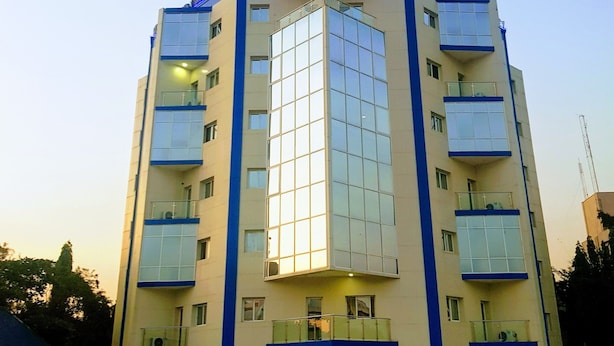 A multi-story building with a central glass facade, balconies on each floor, and a flat roof. - Blue Springs Hotel (Abuja)