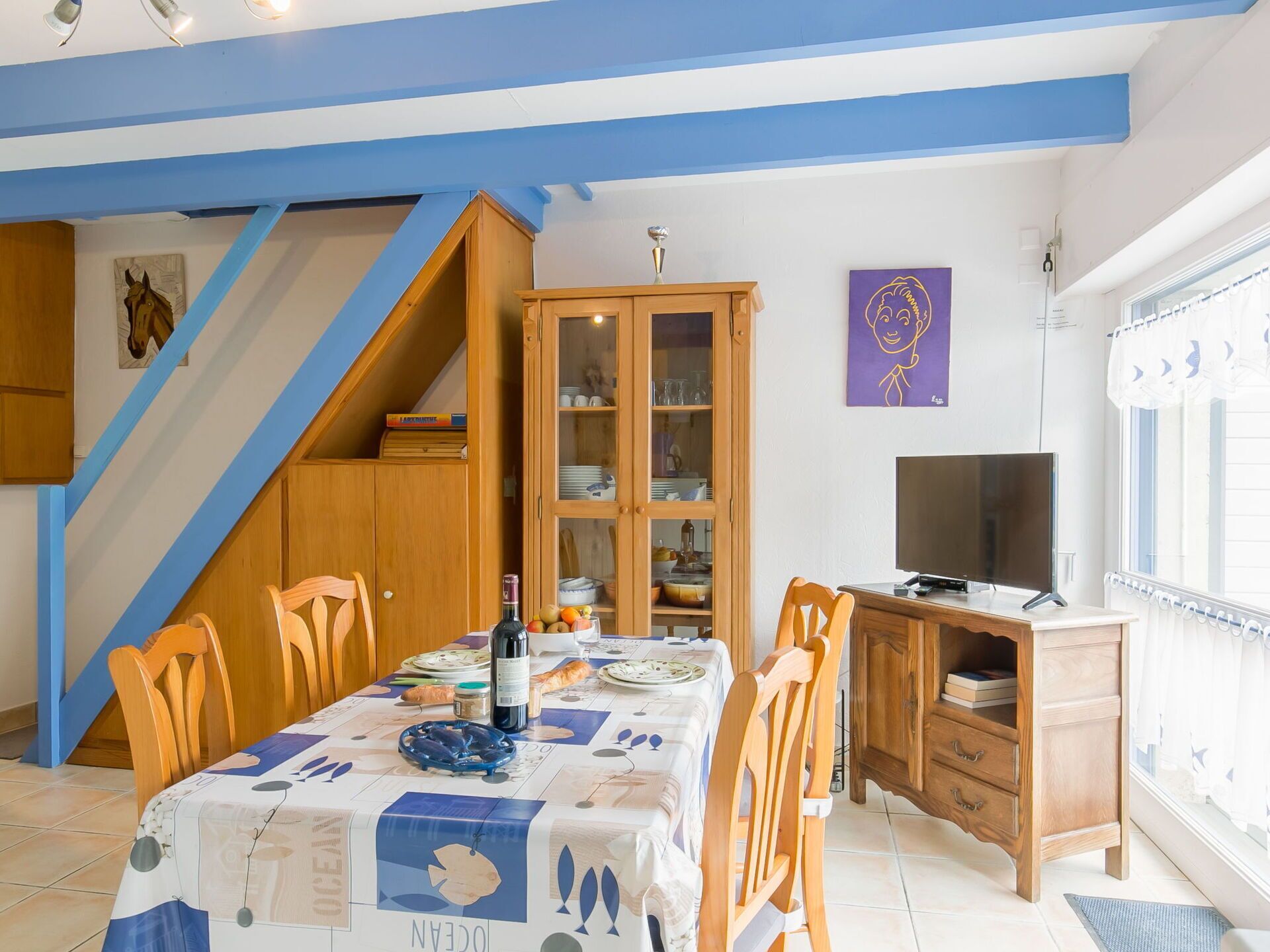 Ein Essbereich mit Tisch für zwei Personen, einer Holzkabine mit Glastüren, einem Fernseher und einem Fenster mit Vorhängen.