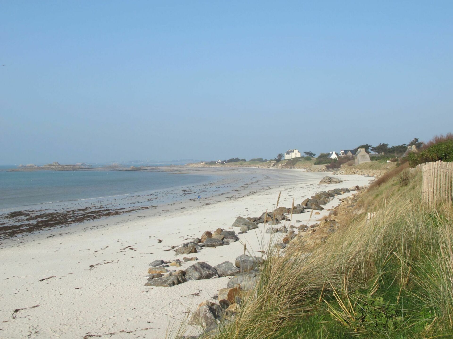 A sandy beach with scattered rocks and a wooden fence.