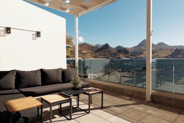 Un espace extérieur moderne, aménagé avec des canapés et des tables, offrant une vue imprenable sur un paysage montagneux et un plan d’eau.
