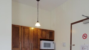 A compact kitchen with wooden cabinets, a microwave, a coffee maker, and a dishwasher. - Water Suites (Charlottetown)