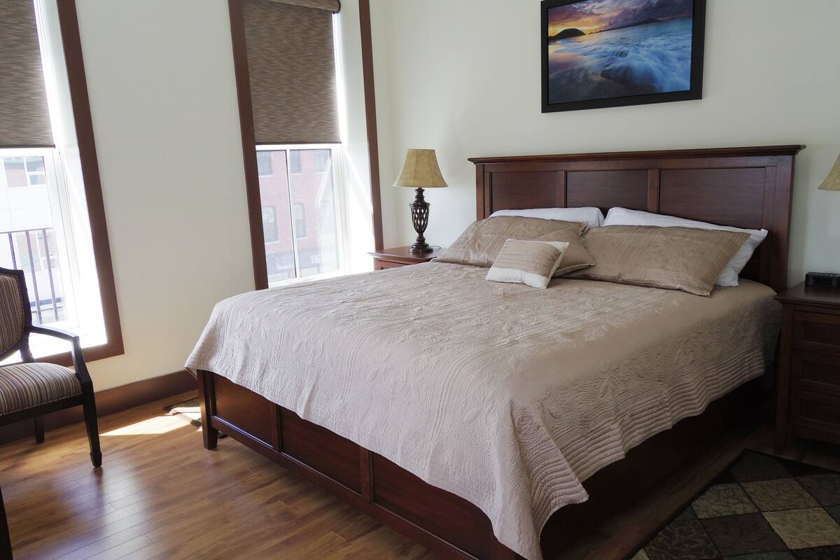 A neatly made bed with a patterned bedspread, a wooden headboard, and two bedside lamps.