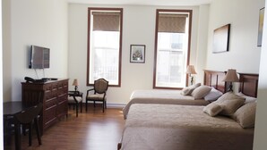 A hotel room with two beds, a desk with a telephone, a chair, and a television on the wall. - Water Suites (Charlottetown)