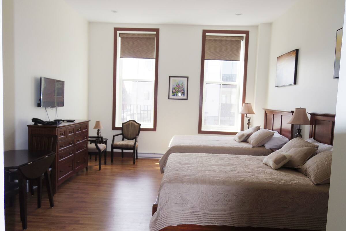 A hotel room with two beds, a desk with a telephone, a chair, and a television on the wall.
