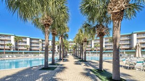 A hotel pool area with palm trees, lounge chairs, and a clear blue sky. - Amalfi Coast - Spacious Condo! (Miramar Beach)