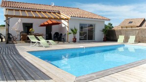 Una piscina con bordo in legno, poltrona prendisole e patio coperto con tavolo e sedie.