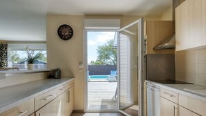 Una cucina moderna con mobili chiari in legno, forno integrato e un'ampia finestra che si affaccia su un giardino con piscina.