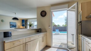 Una cucina moderna con mobili chiari in legno, forno integrato e un'ampia finestra che si affaccia su una piscina.