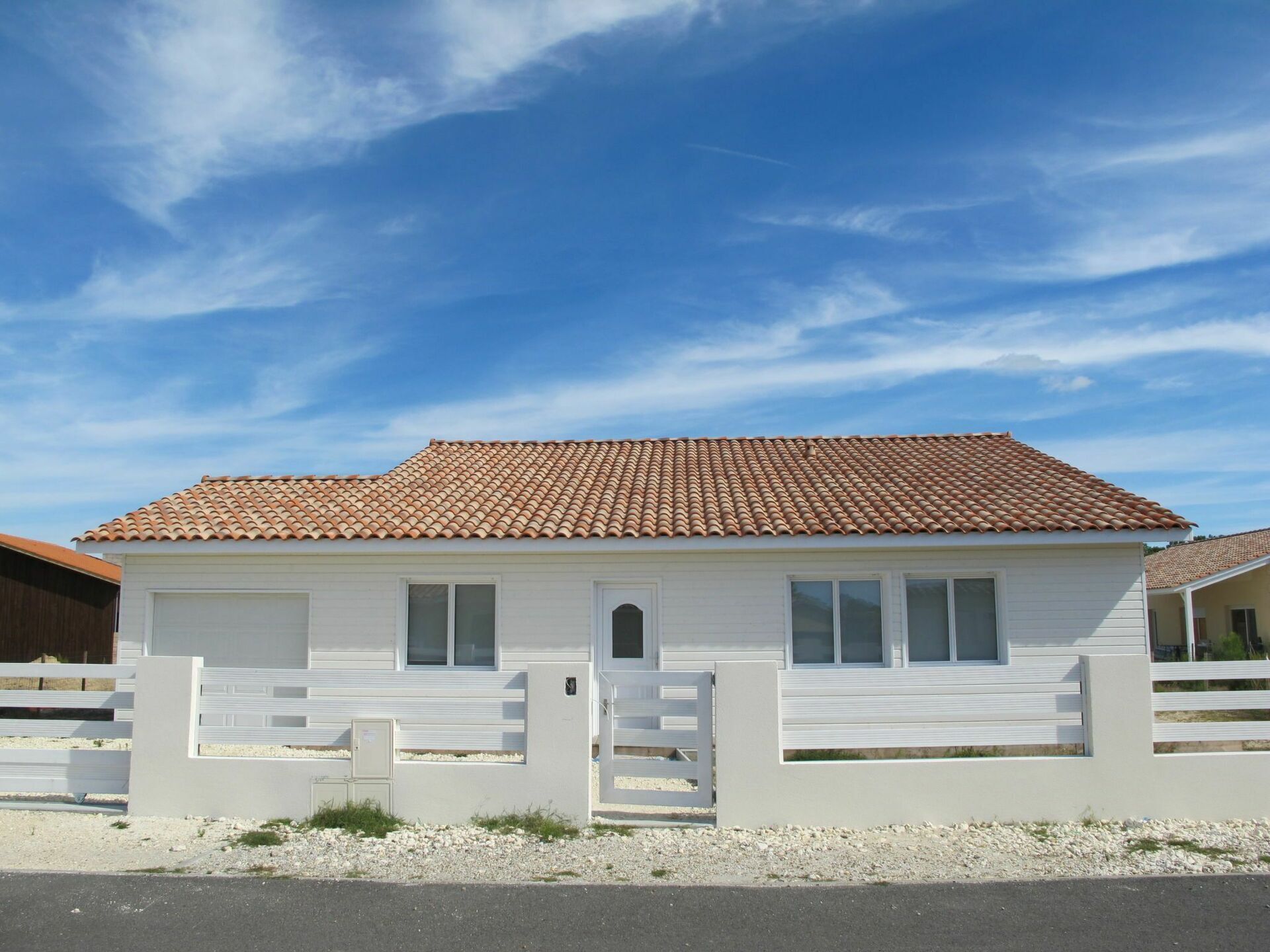 A single-story house with a tiled roof, white exterior walls, and a gated entrance.