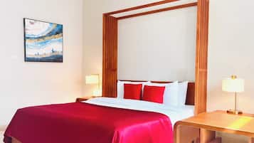 Habitación de hotel con una cama grande, ropa de cama roja, cabecera de madera, mesitas de noche con lámparas y un cuadro en la pared.
