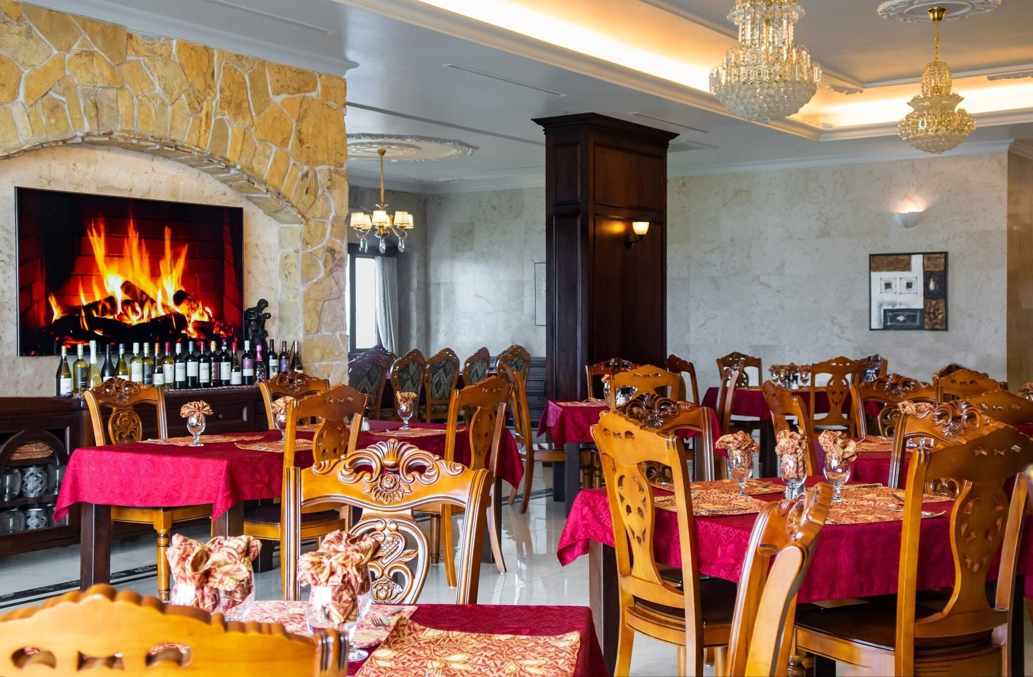 Un restaurante con paredes de piedra, chimenea y varias mesas para comer con manteles rojos.