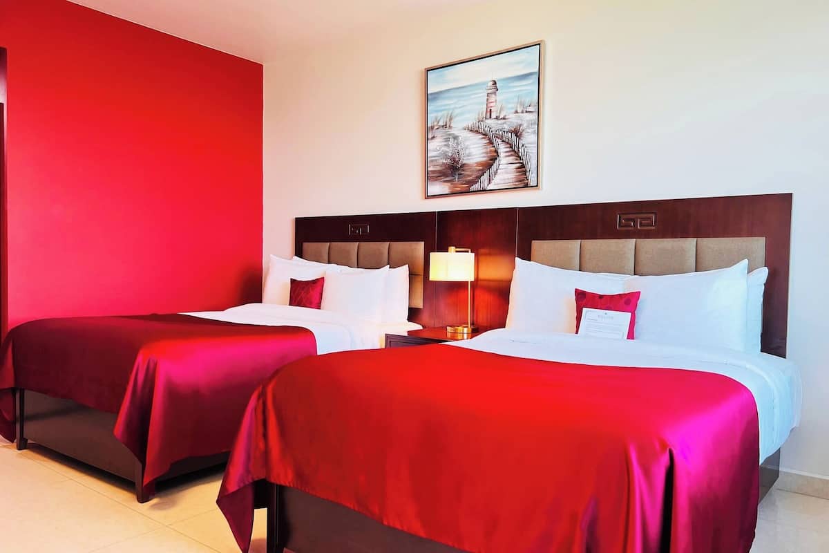 A hotel room with two beds, each with red bedding and white pillows. There is a painting of a lighthouse on the wall above the beds.