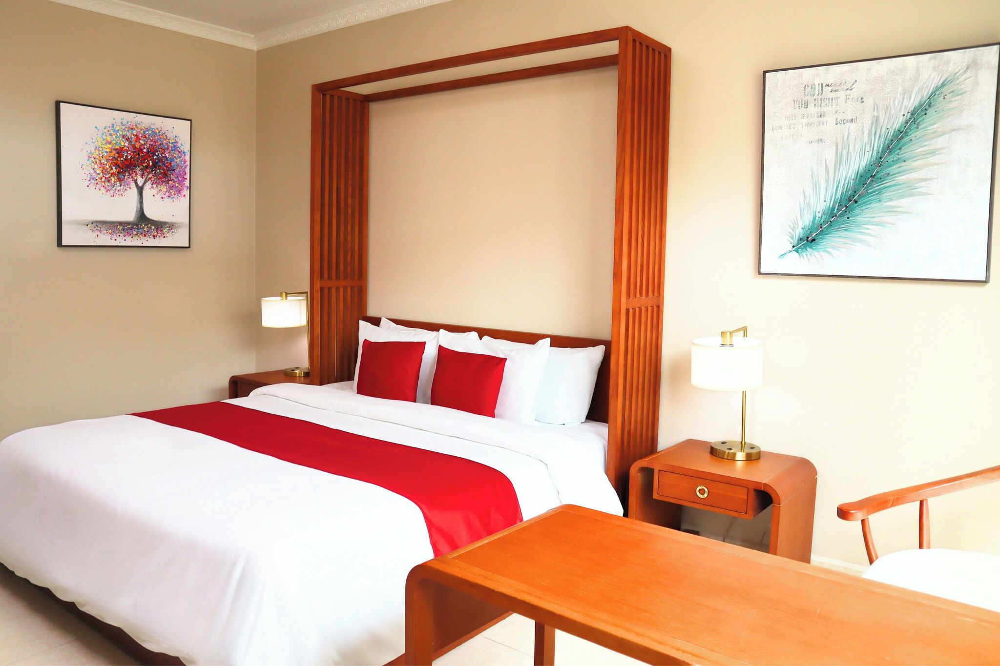 A hotel room with a large bed, red and white bedding, wooden headboard, two bedside tables with lamps, and artwork on the walls.