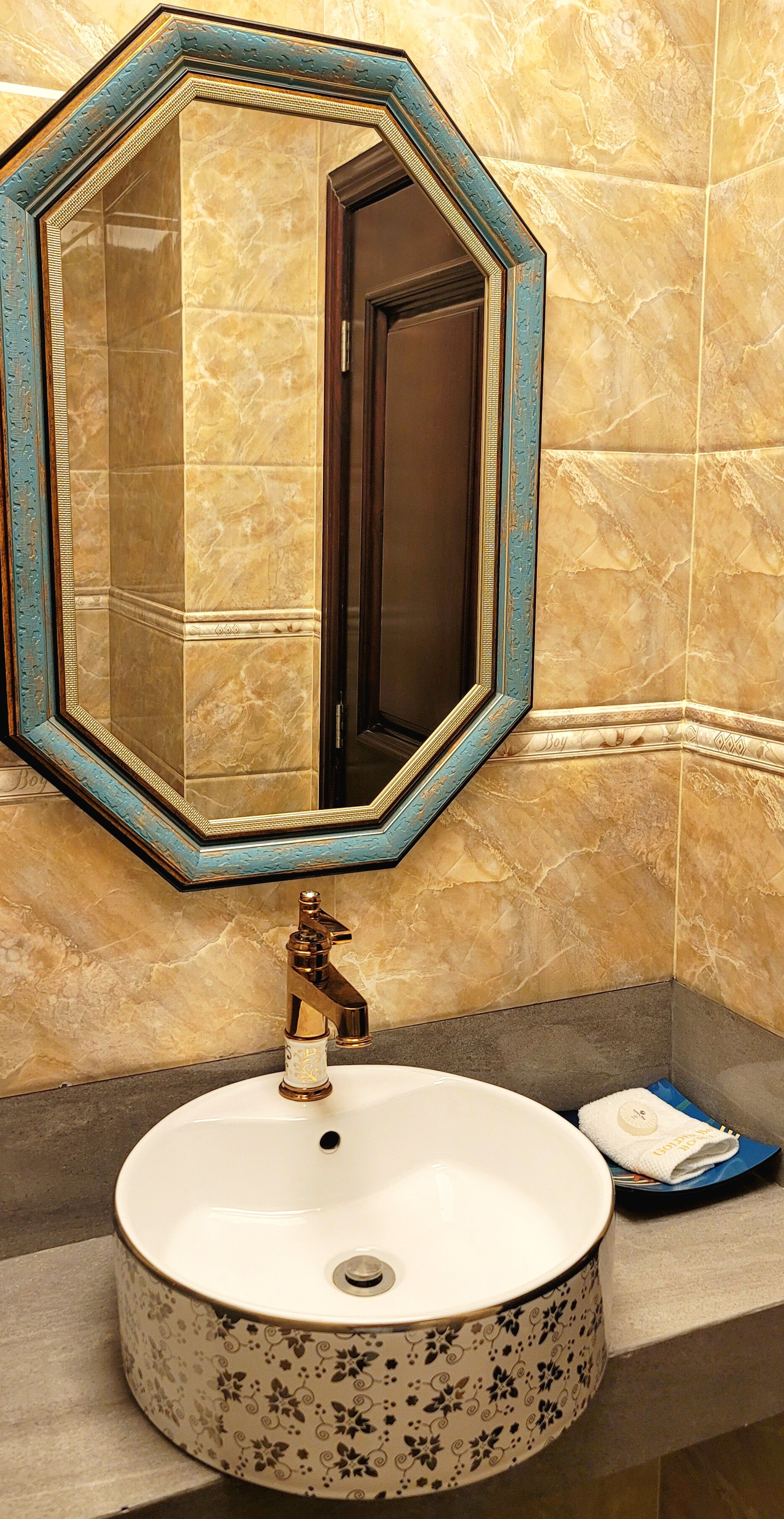 A bathroom with a large octagonal mirror, a round sink with a floral pattern, and a towel on the counter.