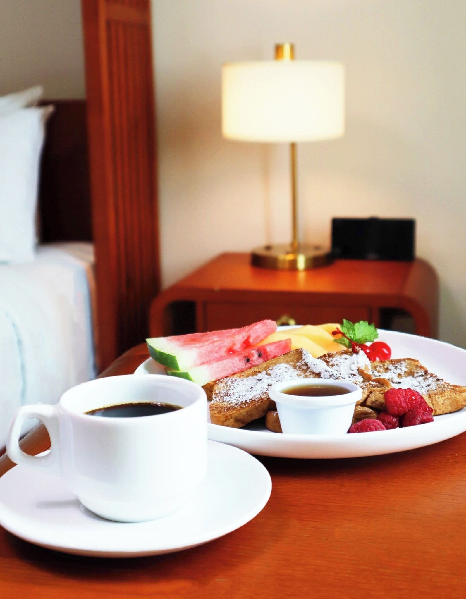 A breakfast setting with a plate of French toast, fresh fruit, and a cup of coffee on a wooden table.
