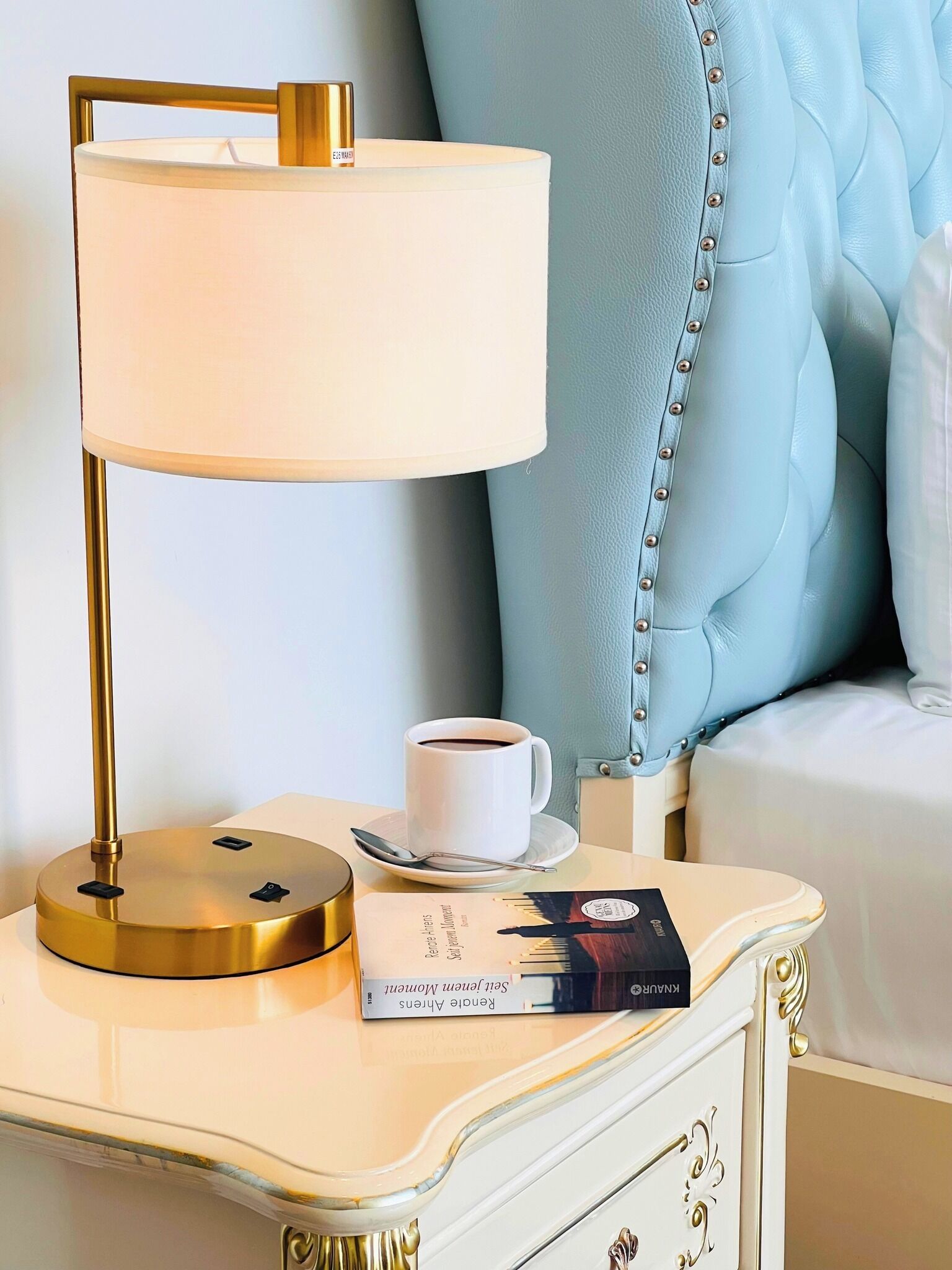 Une table de chevet avec une lampe, une tasse de café et un livre.