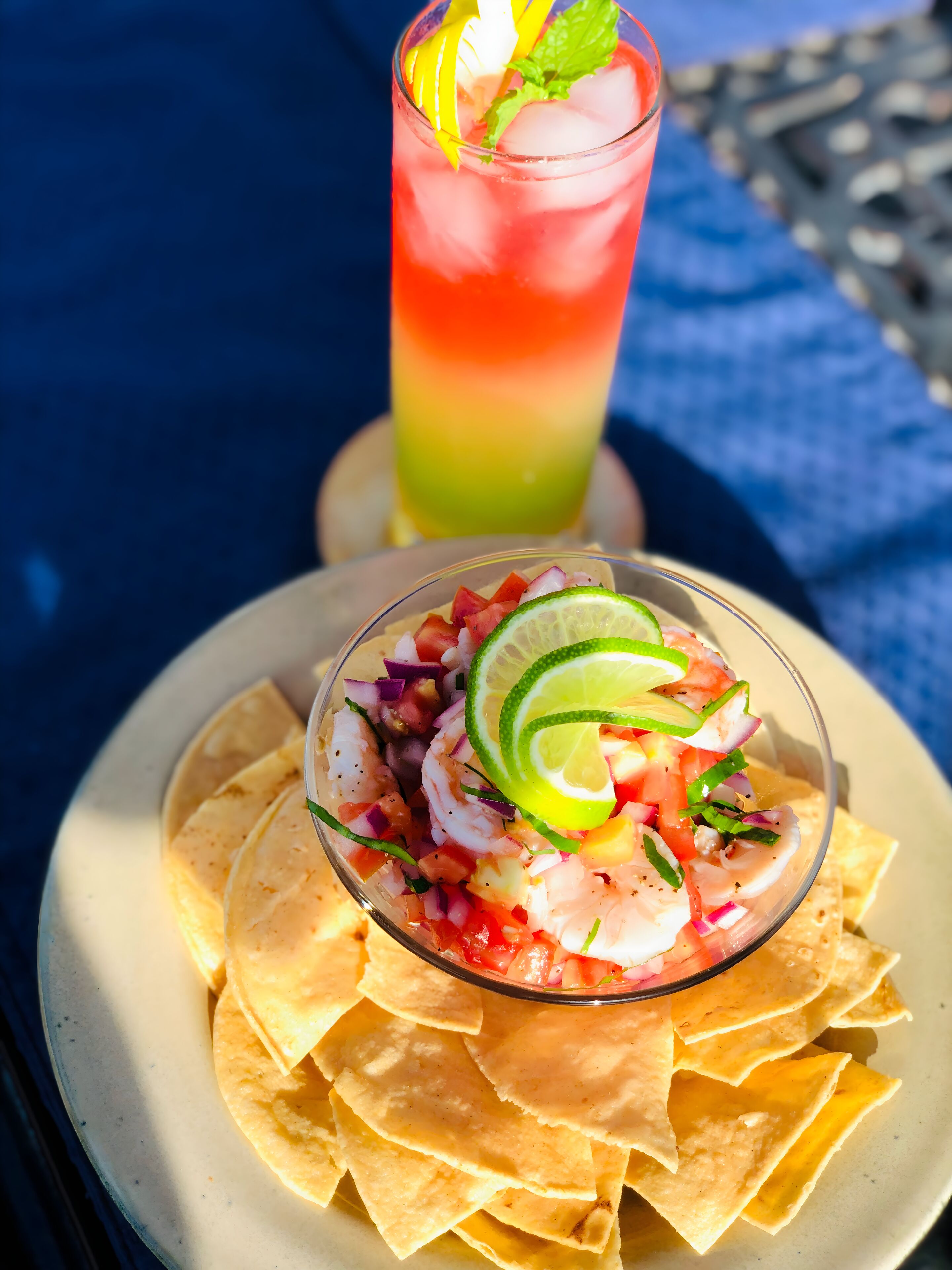 Un plato de totopos con ensalada de mariscos y una bebida colorida.