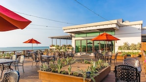 A modern outdoor patio with wooden decking, metal chairs, and red umbrellas. - Golden Bay Hotel by Marine Parade (Belize City)