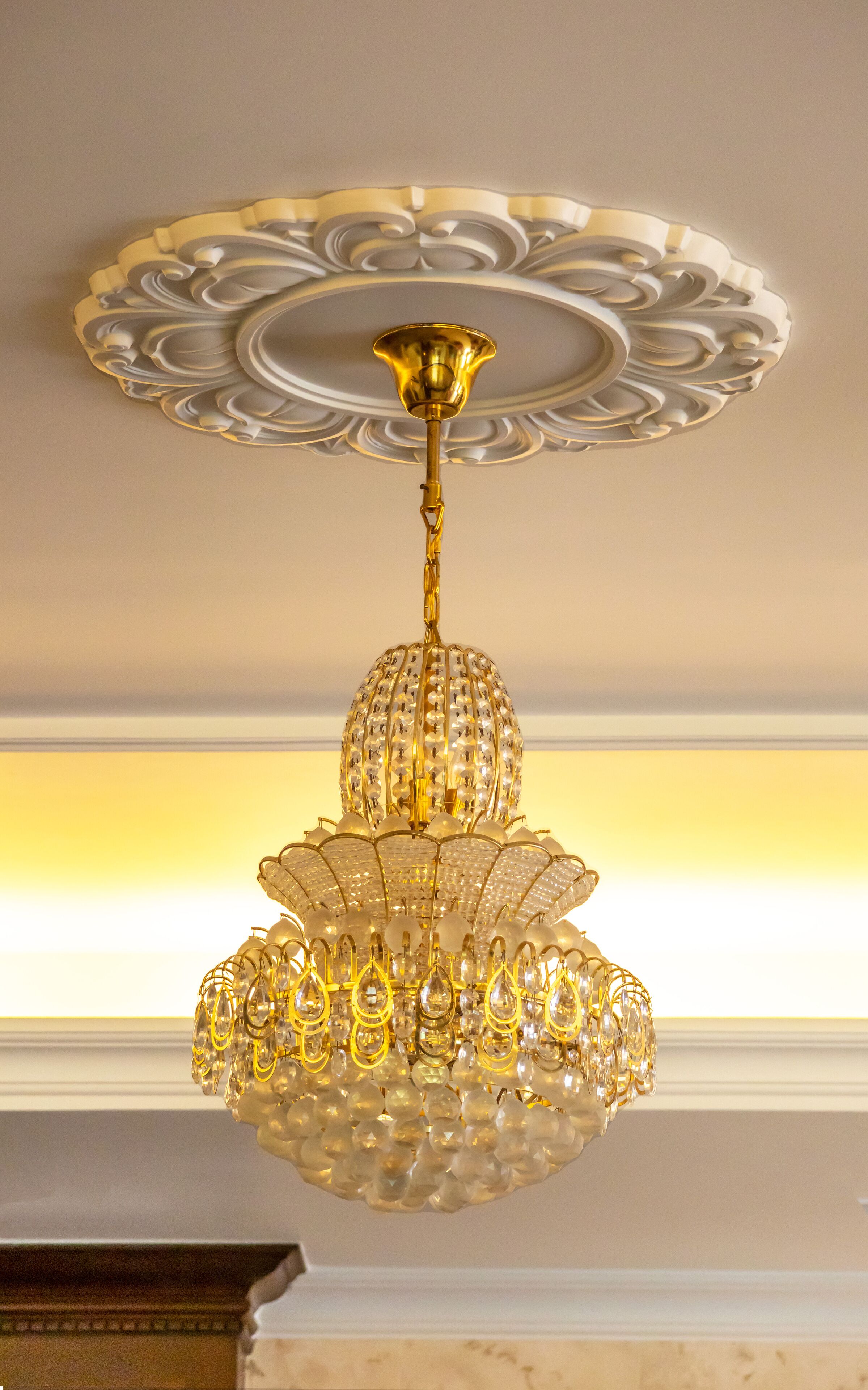 Un candelabro con diseño dorado y adornado con cristales, colgando de un techo ricamente decorado.