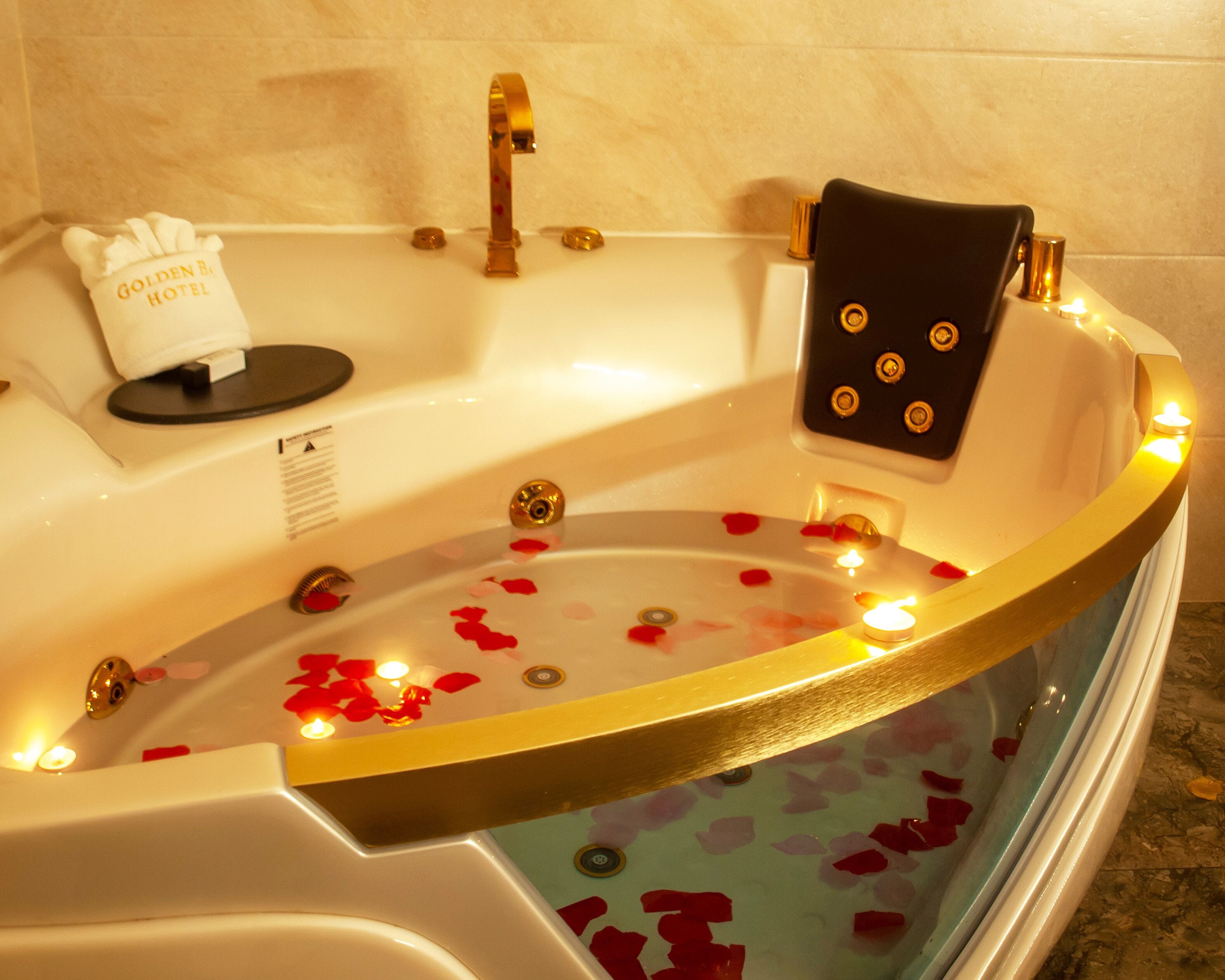 Una bañera con pétalos de rosa y velas, una toalla y una botella de champú.