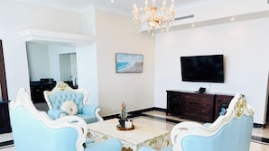 A spacious living room with a light blue sofa set, a marble coffee table, and a dark wooden cabinet with a flat-screen TV mounted above it. - Golden Bay Hotel by Marine Parade (Belize City)