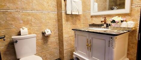 Un baño con inodoro, paredes de mármol, tocador con espejo y toallero.