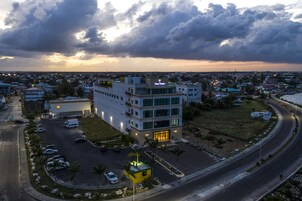 Un edificio de varios pisos con un letrero llamativo, rodeado de un estacionamiento y una carretera curva.