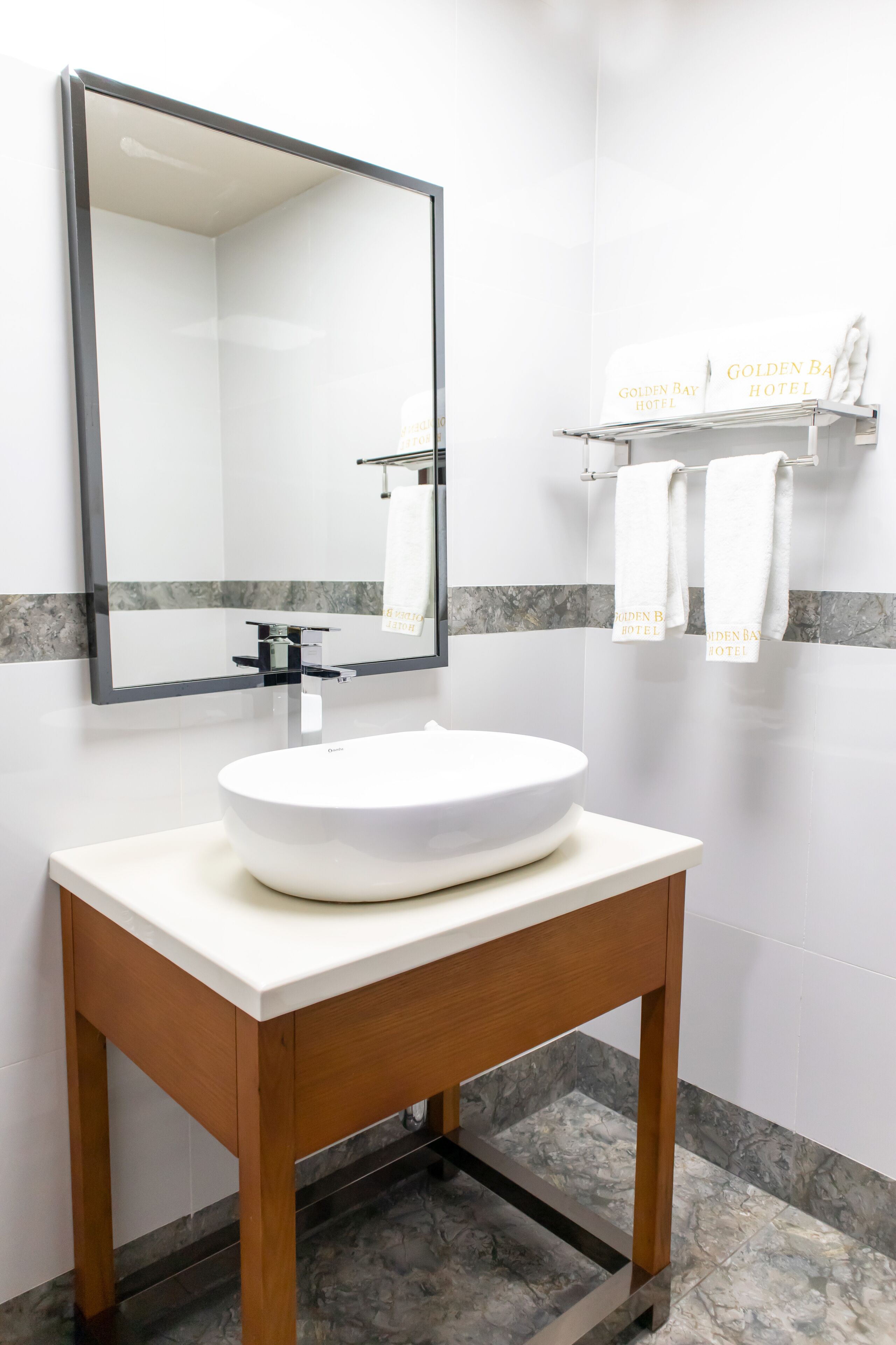 A bathroom with a white sink, a large mirror, and a towel rack with towels.