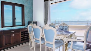 A dining area with a view of the sea, featuring a table set with blue and white chairs, a TV on the wall, and a wine rack. - Golden Bay Hotel by Marine Parade (Belize City)