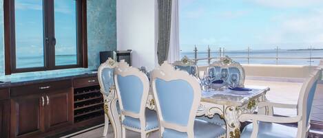 Un comedor con vistas al mar, que incluye una mesa con sillas azules y blancas, un televisor en la pared y una estantería para vinos.