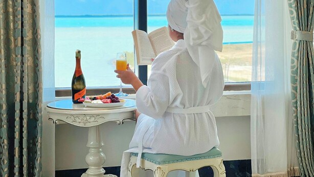 A person reading a book by a window with a view of the sea. - Golden Bay Hotel by Marine Parade (Belize City)