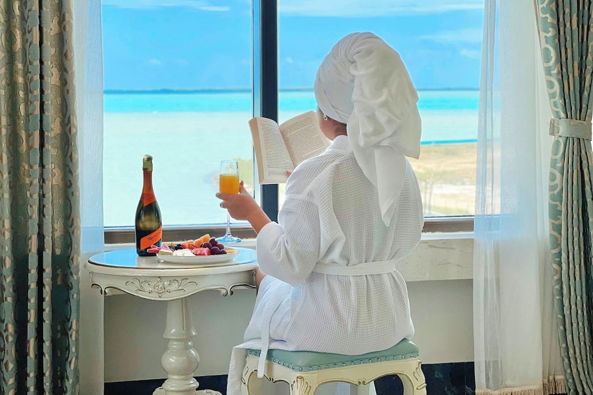 A person reading a book by a window with a view of the sea.