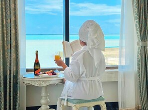 A person reading a book by a window with a view of the sea. - Golden Bay Hotel by Marine Parade (Belize City)