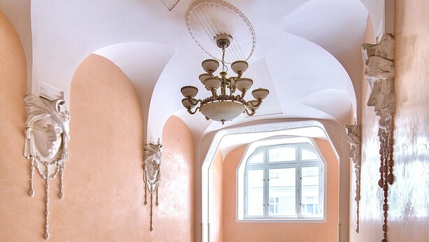 A grand staircase with red carpeted steps leading to a large arched doorway. - Charming river apartment, Castle view, Breakfast incl. (Praha 5)