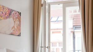 A bedroom with a bed, beige curtains, a window, and a painting on the wall. - Charming river apartment, Castle view, Breakfast incl. (Praha 5)