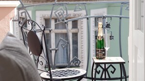 A balcony with a metal chair and a small table, a bottle of champagne, and a view of a building with balconies. - Charming river apartment, Castle view, Breakfast incl. (Praha 5)