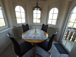 A dining area with a round table, four chairs, a bottle of wine, and a chandelier.